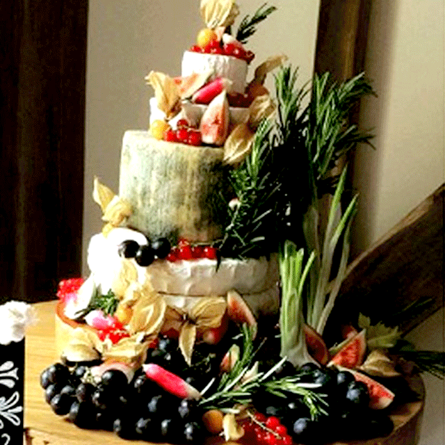 A five tier wedding cake style display of different delicious cheeses, dressed up to the nines with sable grapes, French breakfast radish, spring onions rosemary and physalis
