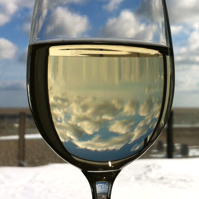 A glass of white wine with blue skies and fluffy white clouds refracted through it leading to our web-form contact page